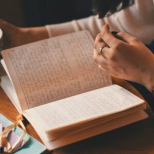 A woman writes in a journal while enjoying a cup of coffee at a wooden table.