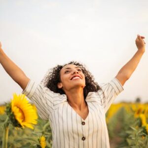 Joyful woman with arms raised in a sunflower field, embracing freedom and happiness.